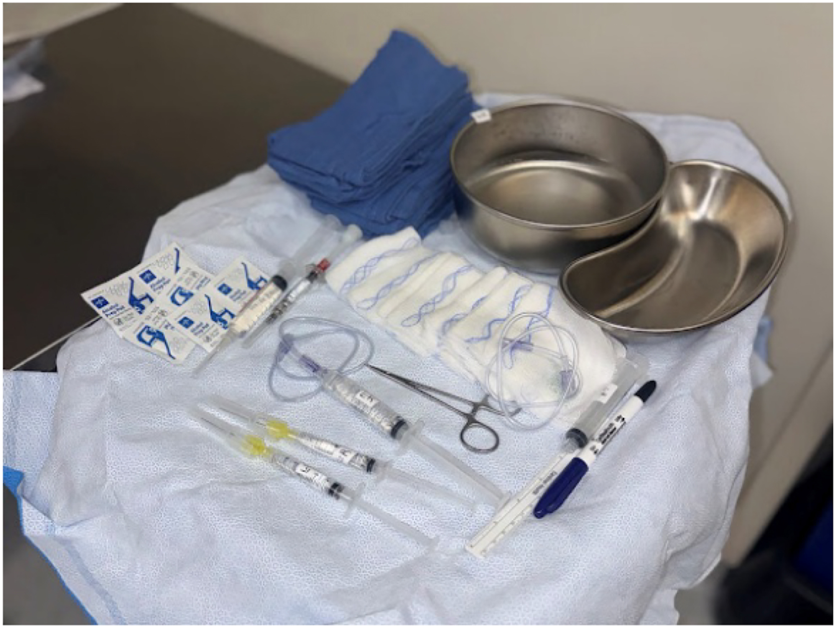 Alt text begins. A clinical photograph depicts a dual-port procedure setup with metal basins, packaged instruments, syringes, tubing, gauze pads, and a marker arranged on a sterile drape. Alt text provided by Elsevier.